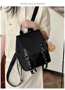 Detail of black nylon backpack featuring silver rivets, drawstring closure and plush pendant