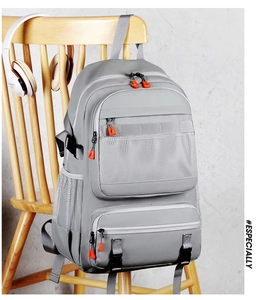 Detail of grey hiking backpack with mesh pocket and orange zippers hanging on a chair