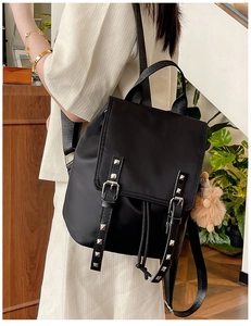 Detail of black nylon backpack with silver studs, drawstring closure and plush pendant