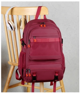 Detail of burgundy hiking backpack with mesh pocket and orange pullers on a wooden chair
