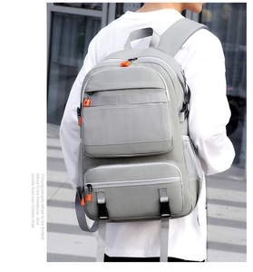 Light gray backpack with orange zipper accents shown on a model in an outdoor setting