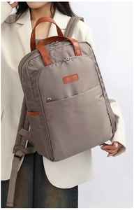 Detail shot of a taupe nylon laptop backpack with brown leather trim shown on model