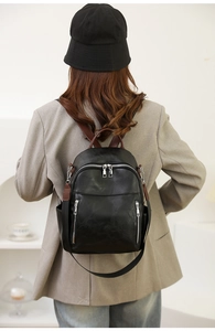 Modischer schwarzer Kunstlederrucksack am Modell mit braunen Riemen und Doppelreißverschluss