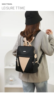 Rear view of a black nylon travel backpack with a beige triangular panel on a female model