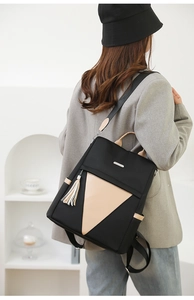 Detail of black nylon backpack featuring beige triangular leather panel and silver tassel
