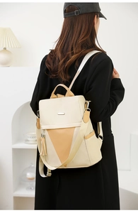 Detail of beige and khaki nylon backpack featuring decorative tassels and smooth zippers