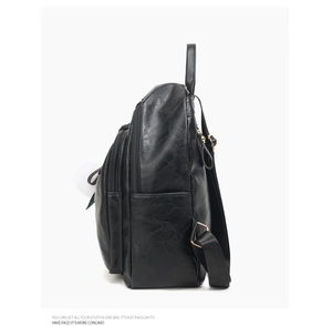 Detail view of black faux leather backpack showing litchi grain texture and side pocket