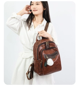 Detail of vintage brown PU leather backpack with dual zippers and white plush pom-pom charm