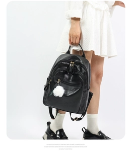 Detail of black leather backpack with layered zippers and white plush ball charm