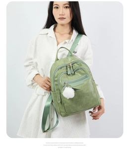 Close-up of sage green soft leather backpack with white pompom and dual zippers