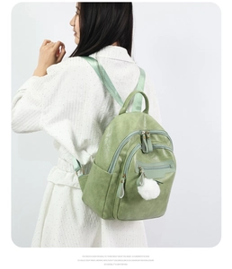 Detail view of mint green PU leather backpack with plush ball charm on female model