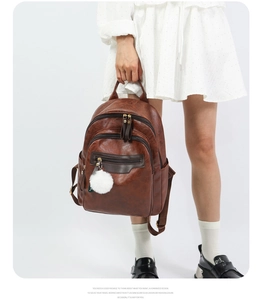 Detail of vintage brown soft leather backpack with a decorative white plush ball charm