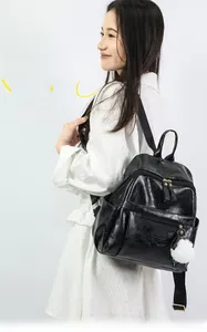 Detail of black PU backpack featuring multiple zipper layers and a white fur ball pendant