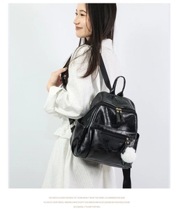 Side view of trendy black PU leather backpack for women featuring a white fuzzy pompom charm