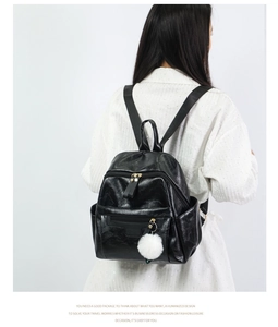 Detail view of black PU leather backpack featuring a front zipper and white fur ball charm