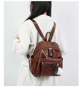 Side view of dark brown PU leather backpack with plush pendant worn on white dress