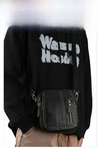 Detail of black pebbled leather crossbody bag featuring contrasting yellow stitching