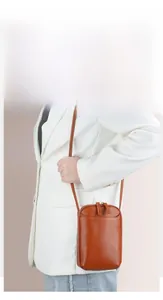 Brown litchi grain leather crossbody phone bag with double zippers worn on a white blazer