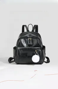 Detail of black PU leather backpack featuring golden zippers and a white pompom charm