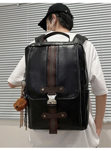 Close-up of black PU leather backpack with vintage metal buckles and bear keychain