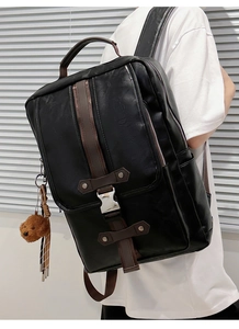 Detail of black PU leather backpack with brown vertical trim and teddy bear charm