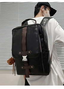 Detail of black PU leather backpack featuring brown leather straps and a plush bear charm