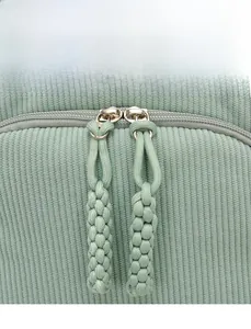 Detail of green corduroy backpack showing smooth zipper and woven decorative puller