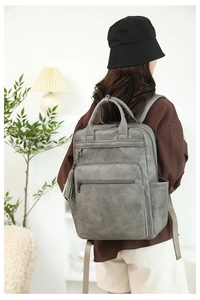 Detail of dark grey faux leather backpack featuring multiple zippers and side tassel charm