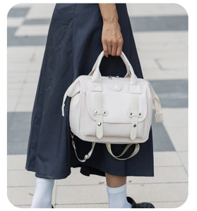 Close-up of cream canvas mommy bag featuring dual leather buckles and circular logo patch