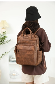 Detail of brown PU leather backpack featuring side tassel and multi-pocket structure