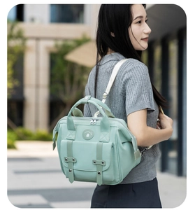 Detail of mint green mommy bag featuring round logo and decorative double buckle straps