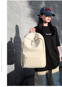Asian model holding a minimalist beige Oxford cloth backpack against a brick wall