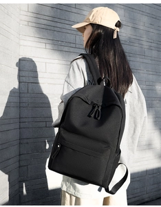 Side view of a minimalist black oxford fabric backpack worn by a model in daylight