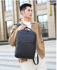Man carrying black leather business laptop backpack walking in front of a building