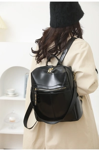 Detail of glossy black leather backpack with gold zippers shown on a model's back
