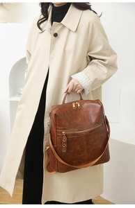 Detail view of brown leather backpack with metal zippers and side eyelet accents on a model