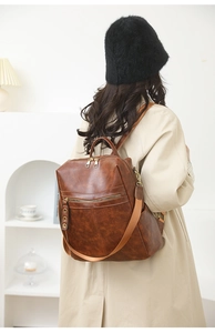 Rear view of brown vintage PU leather backpack with wide straps on a beige trench coat