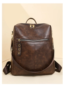 Detail of dark brown leather backpack showing gold zippers and wide shoulder straps