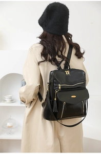 Detail of a vintage black PU backpack with gold zippers and tassel on a model in a trench coat
