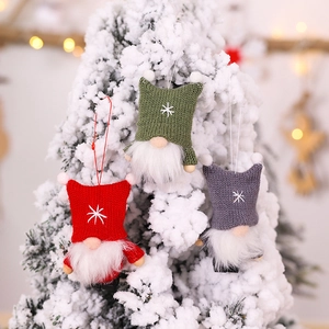 Trois gnomes de Noël tricotés en rouge, vert et gris suspendus au sapin enneigé