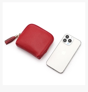 Red pebbled leather mini pouch with long tassel and zipper, shown next to phone for scale