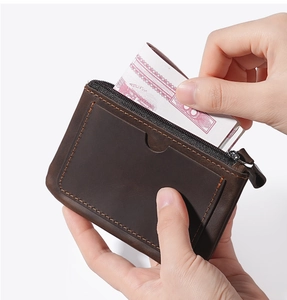 Detailed view of hand inserting bills into a dark brown leather wallet with orange stitching