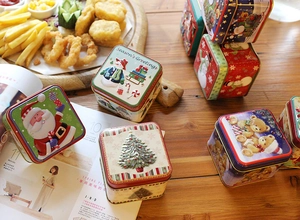 Detailed view of square Christmas tin boxes with embossed Santa and snowman patterns