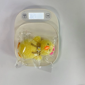 Pulcino di peluche giallo pasquale con fiore rosa su bilancia digitale pesando 82,1g