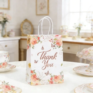 Floral gift bag detail with Thank You gold foil text and white twisted handle on a table
