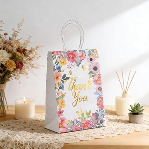 Floral gift bag with gold Thank You stamp and white handles on a rustic table