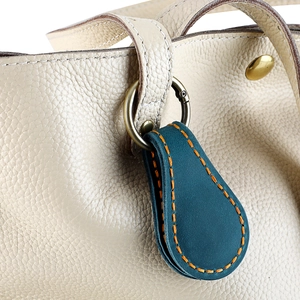 Détail d'une étiquette en cuir sarcelle avec couture orange sur un sac en cuir beige