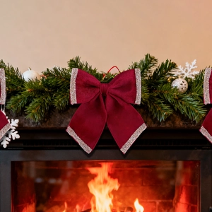Red velvet Christmas bow with silver glitter edges on festive pine wreath near fireplace