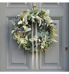 Detail of Christmas wreath with flocked leaves, pine cones, and blue berries on a gray door