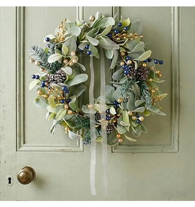 Close-up of a Christmas wreath with green leaves, berries, and pinecones on a green wooden door